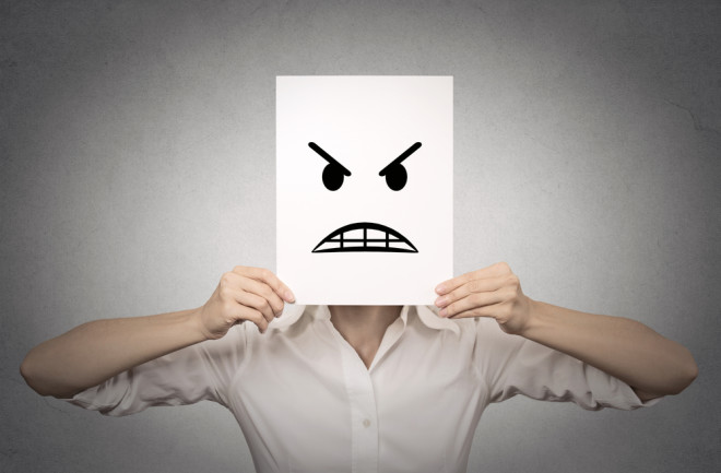 woman holding an angry face drawn on paper in front of her face