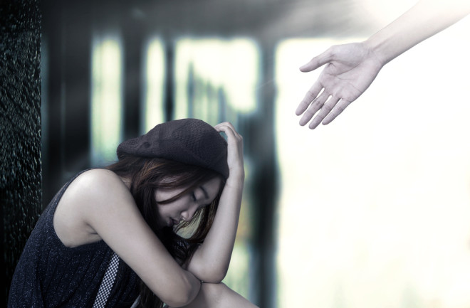 Portrait of stressful teenage girl sitting on the floor with a hand coming out from bright background offers help 