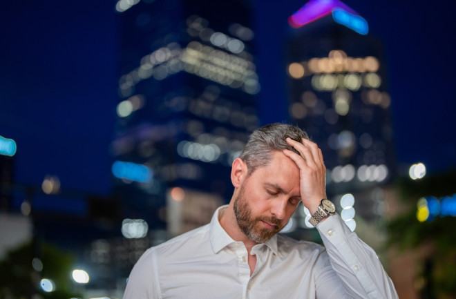 man holding his head stressed in the city