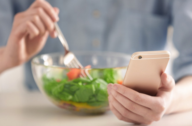 Woman eating a salad and logging meal calories Noom app concept - shutterstock