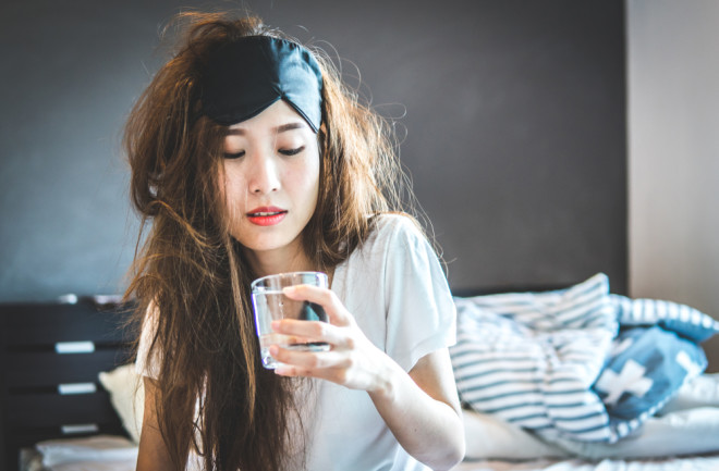 woman with sleep mask and glass of water, trying to cure a hangover