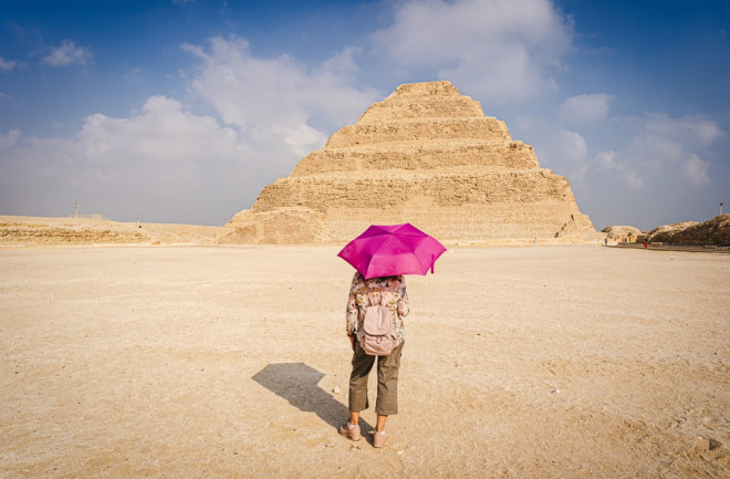 View of a woman with a purple umbrella watching the scale pyramid of Djoser in the Saqqara necropolis. 