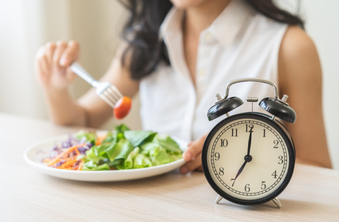 woman eating with a clock, representing intermittent fasting