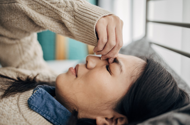 One woman, Japanese woman having headache while lying on bed in her bedroom at home.