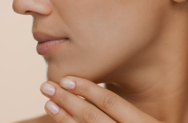 Extreme close-up shot of young woman with perfect skin strokes her jaw line and chin on beige background | Smooth skin and beauty care commercial concept